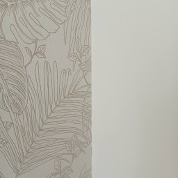 Remonty i wykończenia- Wojciech Rogus - Ściana z tapetą w tropikalne liście i gładka, pomalowana na jasny odcień. Kontrast faktur i wzorów. Minimalistyczny design wnętrza.