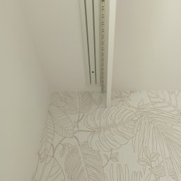 Remonty i wykończenia- Wojciech Rogus - Biała listwa sufitowa z oświetleniem LED, zamontowana przy ścianie z tapetą w motywy roślinne. Ujęcie z dołu, widoczny fragment sufitu i ściany.