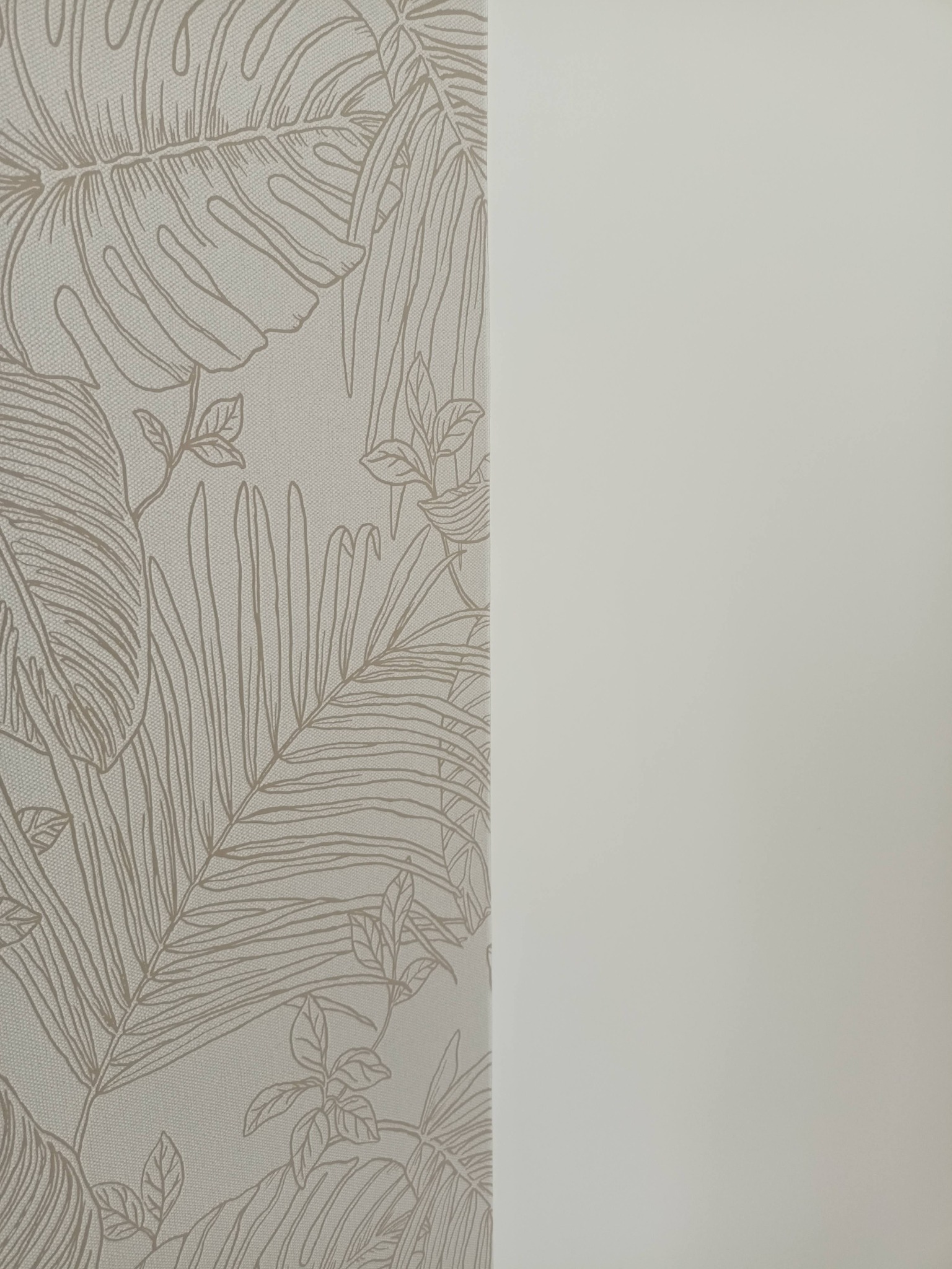Ściana z tapetą w tropikalne liście i gładka, pomalowana na jasny odcień. Kontrast faktur i wzorów. Minimalistyczny design wnętrza.