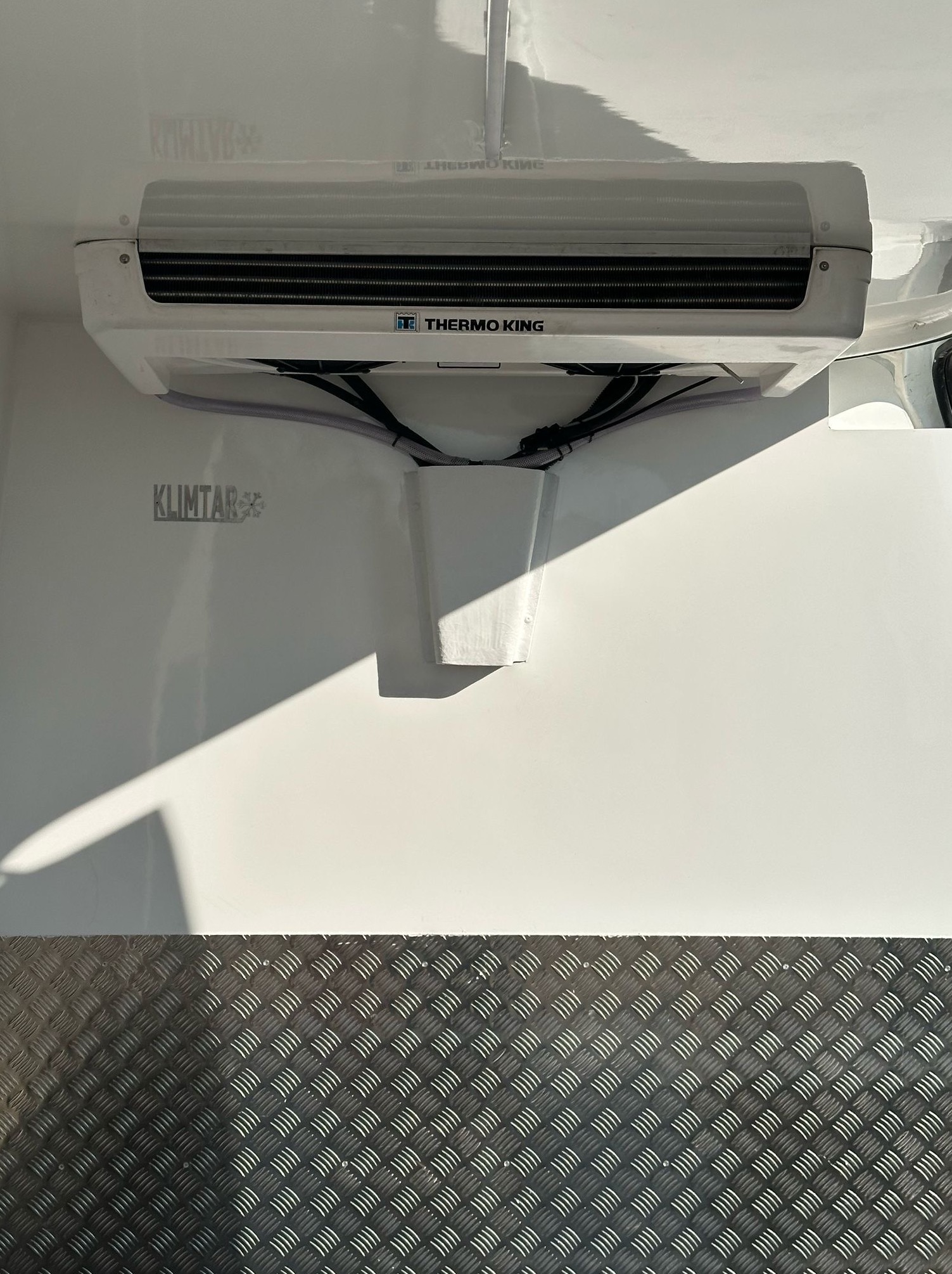 Agregat chłodniczy Thermo King zamontowany w przestrzeni ładunkowej pojazdu, widoczna metalowa podłoga z fakturą rombów i logo Klimtar na ścianie.