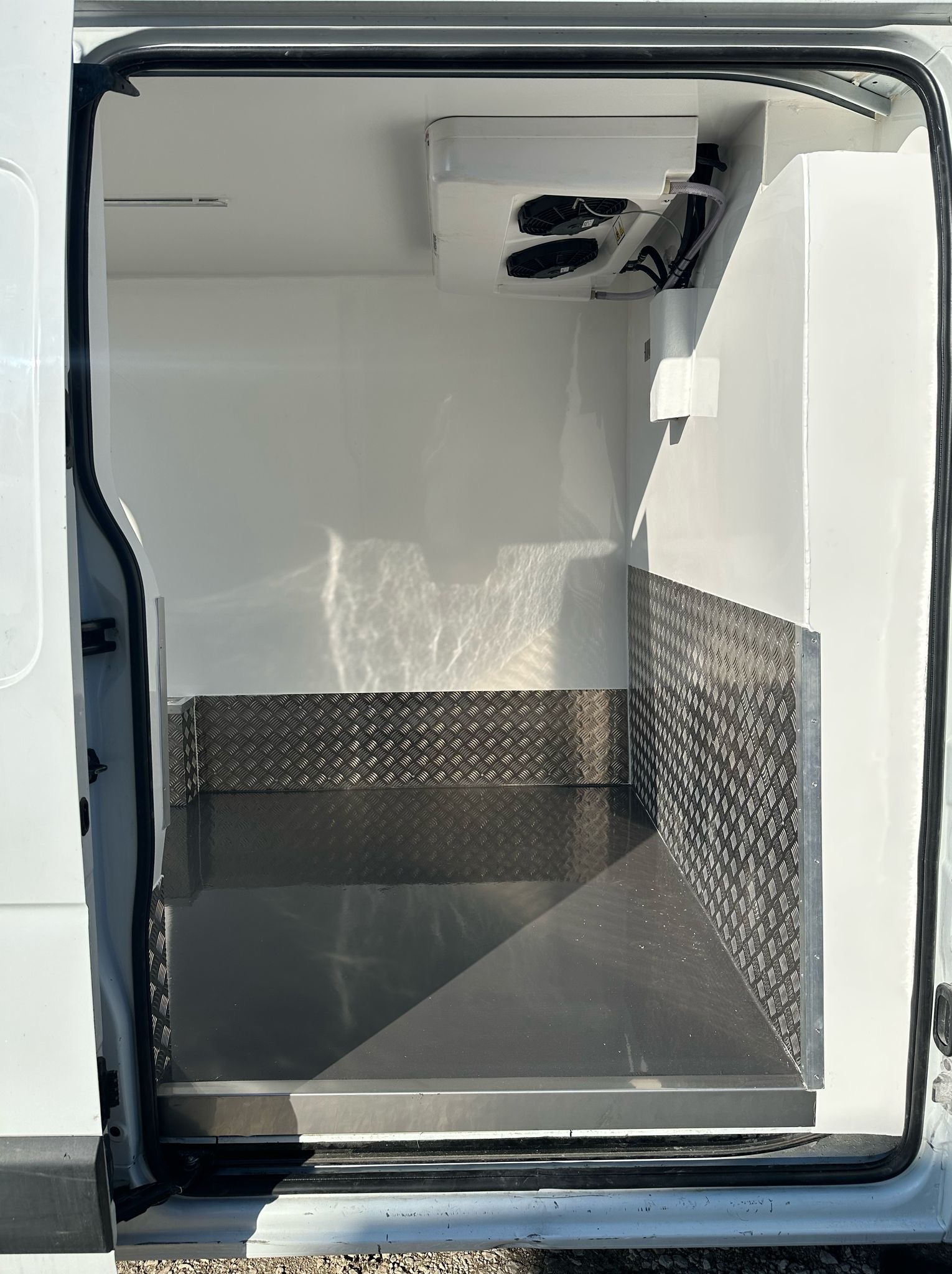 Wnętrze chłodni samochodowej z widocznym agregatem chłodniczym i aluminiową podłogą.