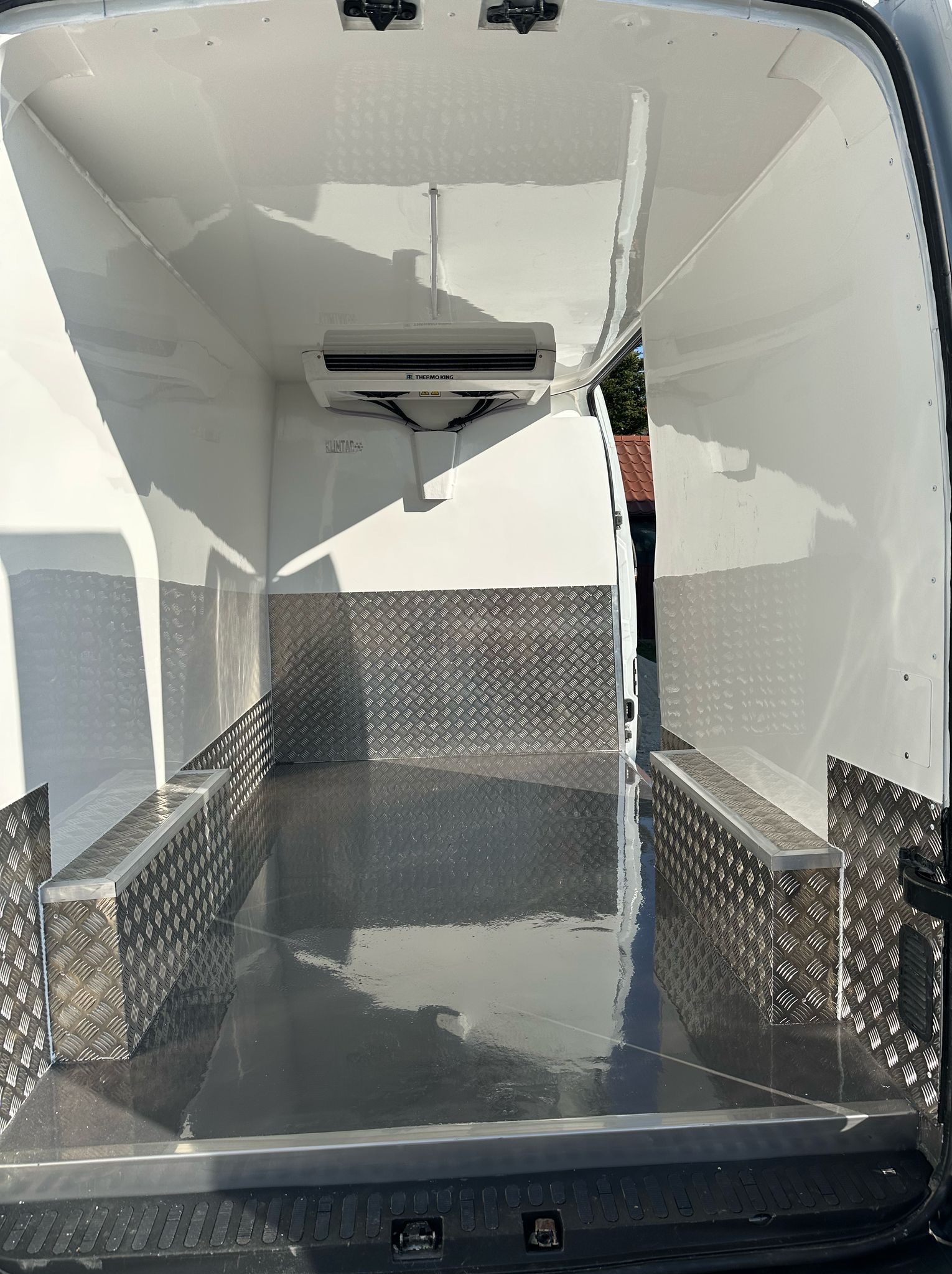 Wnętrze furgonetki chłodniczej z zamontowaną jednostką chłodzącą Thermo King, wyłożone blachą aluminiową ryflowaną, widok od tyłu.