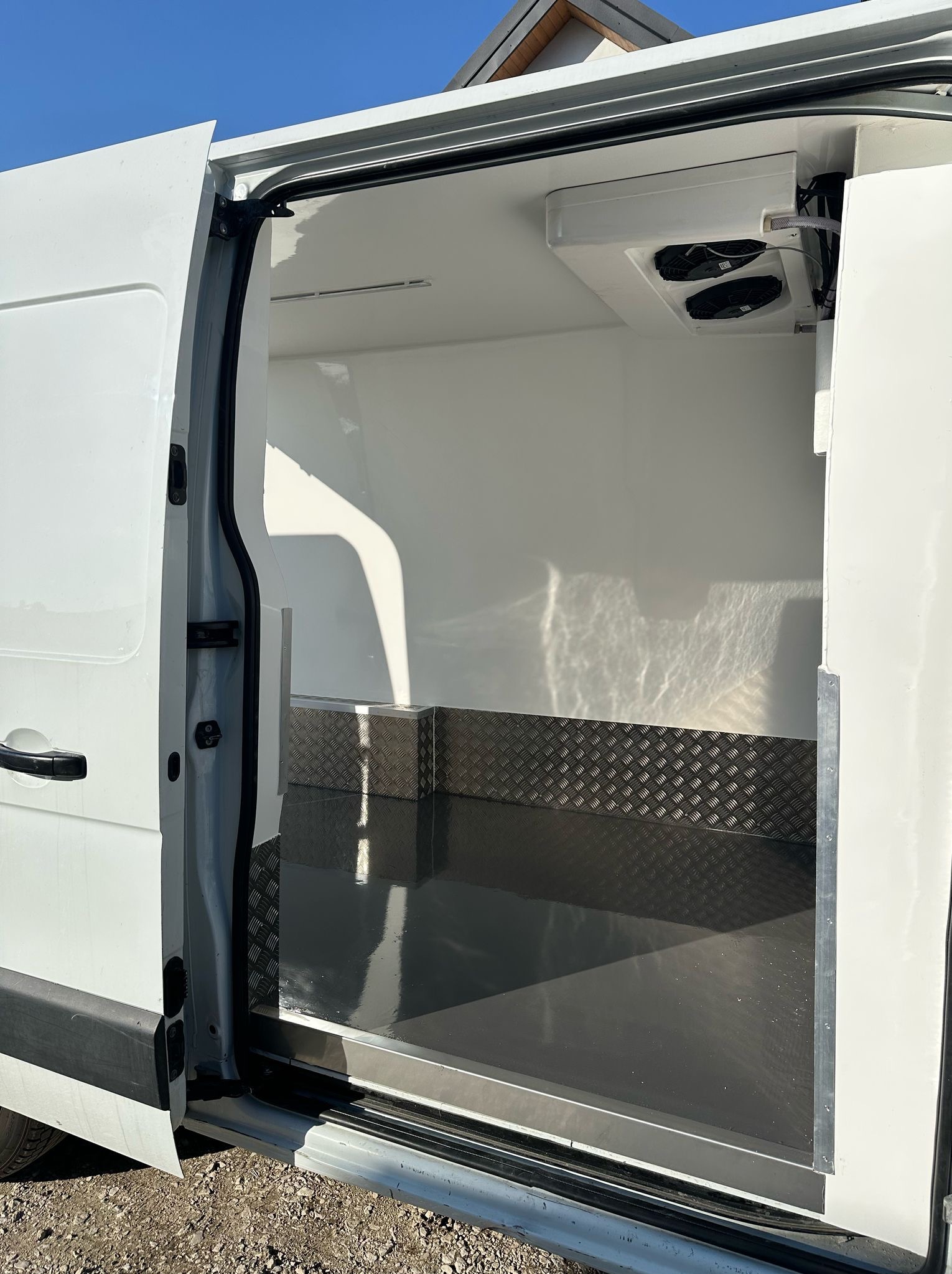 Wnętrze furgonetki chłodniczej z otwartymi drzwiami bocznymi, widoczna zabudowa izolacyjna, agregat chłodniczy z dwoma wentylatorami zamontowany pod sufitem oraz metalowa podłoga z antypoślizgową...