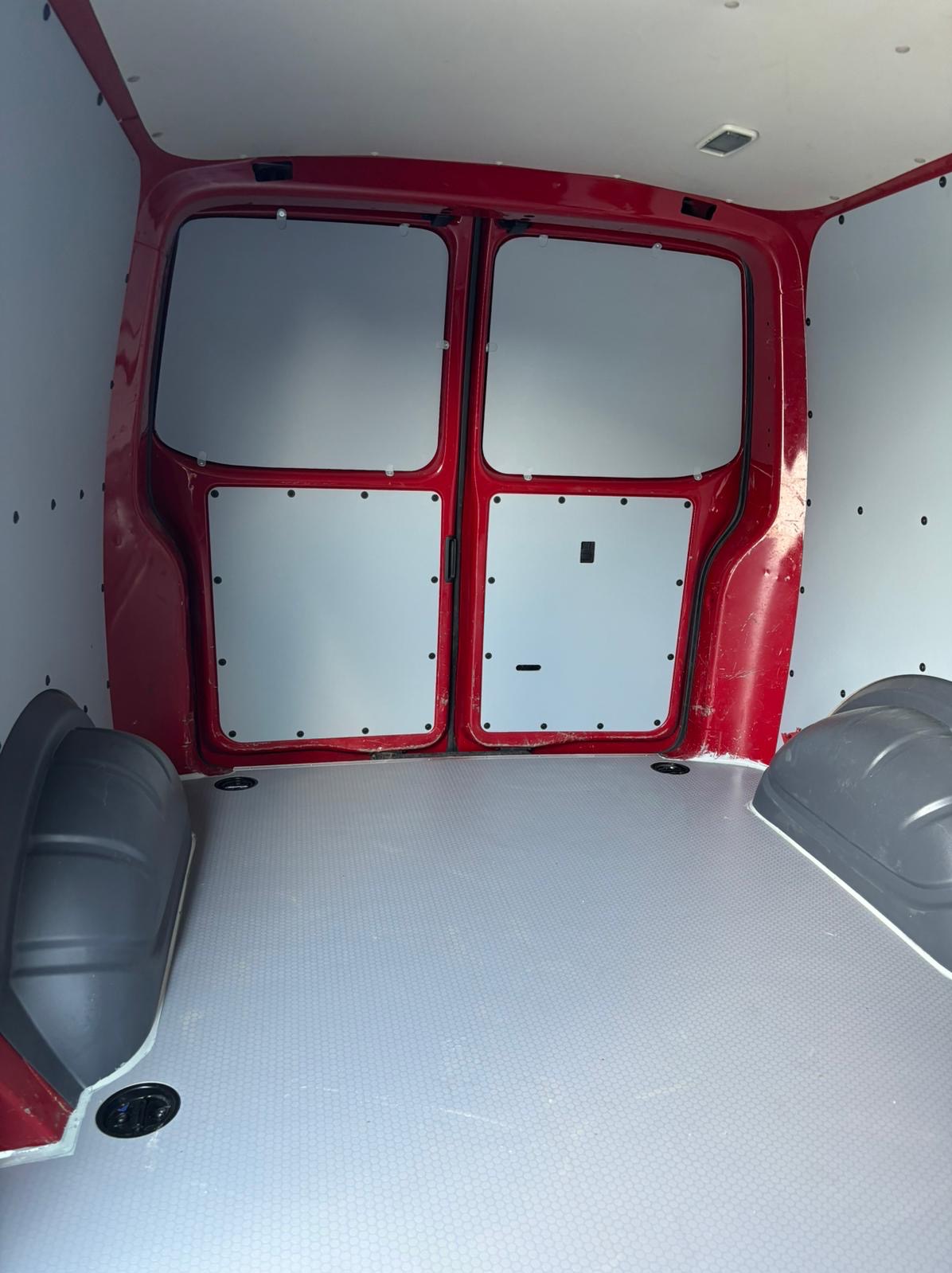 Wnętrze czerwonego furgonetki z szarą podłogą o wzorze plastra miodu i szarymi panelami bocznymi zabezpieczonymi czarnymi nitami.