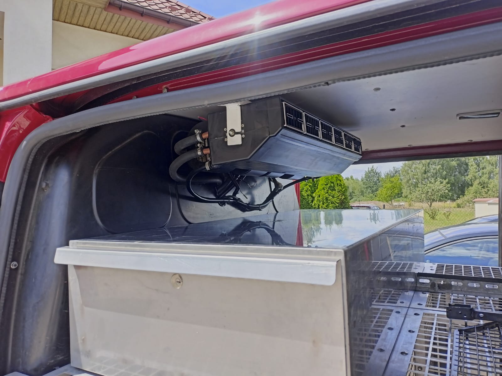 Zamontowany system klimatyzacji w przestrzeni ładunkowej pojazdu, widoczne przewody i kratka wentylacyjna, na tle zabudowy i otoczenia zewnętrznego.