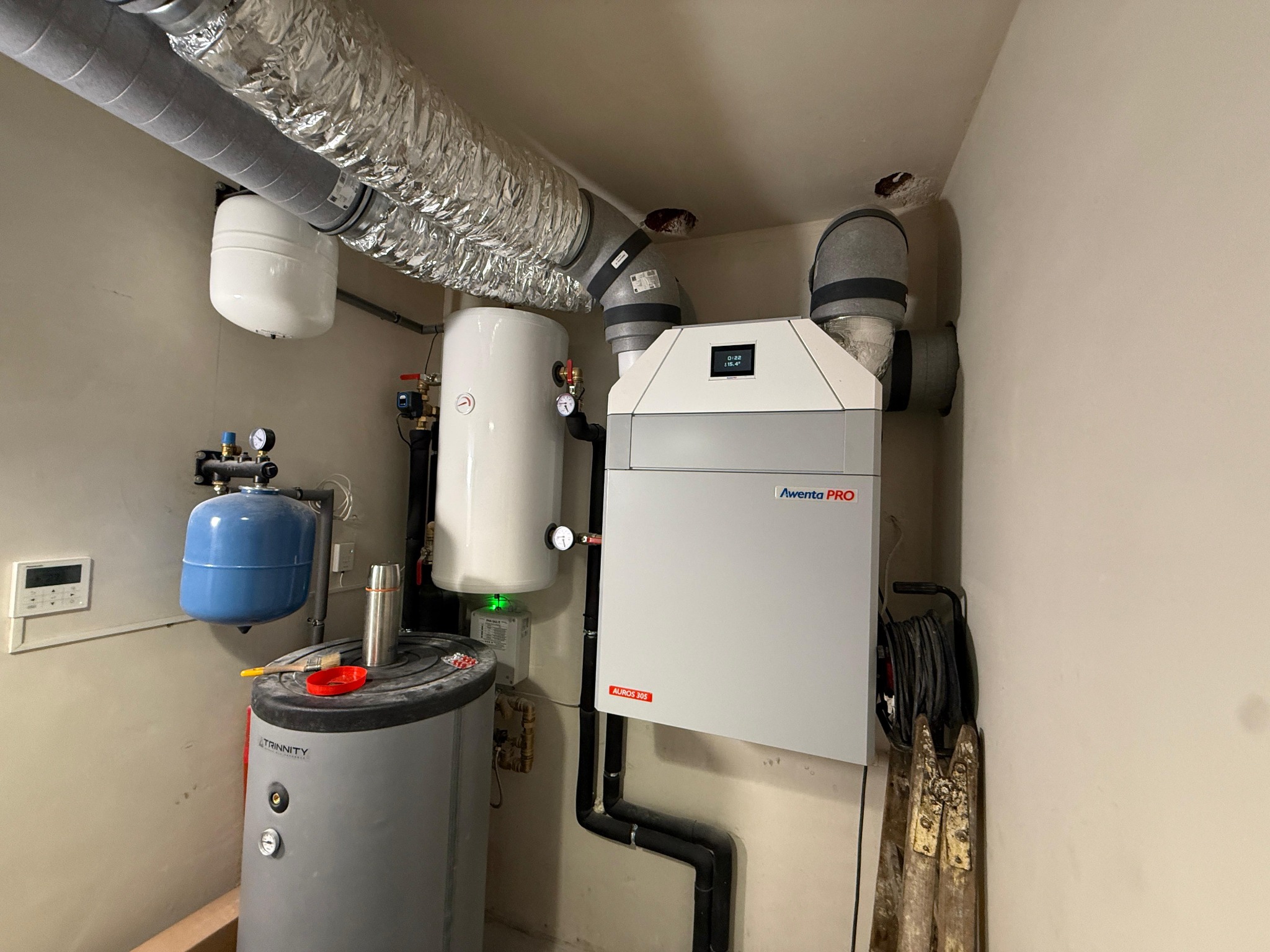 Zestaw urządzeń: rekuperator Aventa PRO, zbiornik buforowy Trinitty, naczynia przeponowe. Instalacja w pomieszczeniu technicznym z rurami wentylacyjnymi.