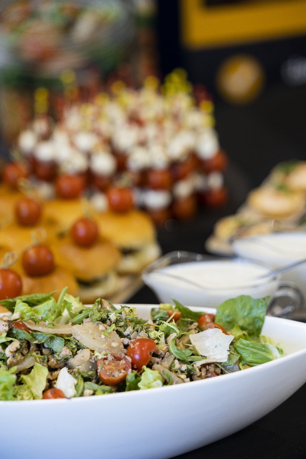 Elegancki bufet w Warszawie: sałatka w białej misie na pierwszym planie, w tle mini burgery i koreczki. Profesjonalny catering na imprezę firmową.