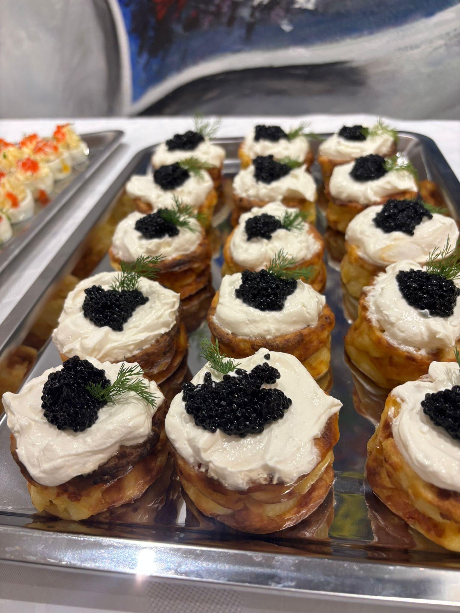 Eleganckie mini bliny z kawiorem i kremowym serem na srebrnej tacy, dekorowane koperkiem. Idealne na wykwintny catering.