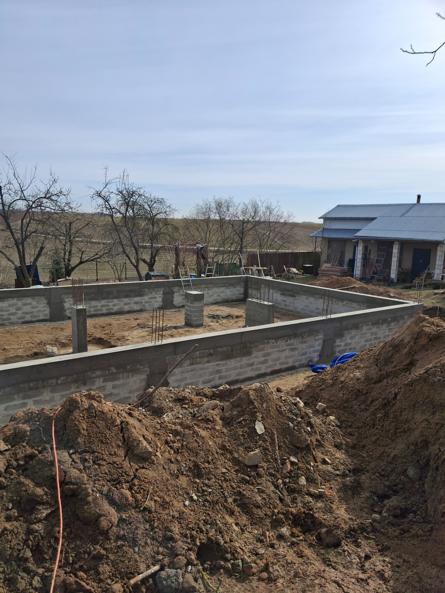 Fundamenty zbrojone, bloczki betonowe, widok z ziemi w Lublinie. Etap budowy domu z widocznym zarysem ścian i słupów nośnych. Niebieskie rury w tle.