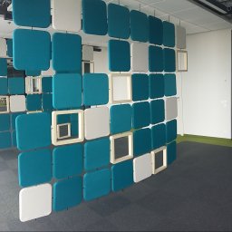 E3 Office Interiors - Panelowa ścianka działowa z turkusowych i białych kwadratów z zaokrąglonymi rogami, niektóre z ramkami, tworząca ażurową konstrukcję w biurze.