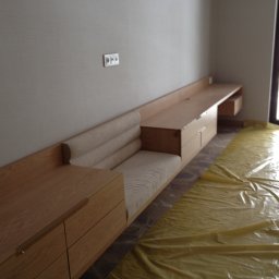 E3 Office Interiors - Jasne drewno i tapicerka w zabudowie meblowej z szufladami i siedziskiem, przykryte folią ochronną. Minimalistyczny design, nowoczesne wykończenie.