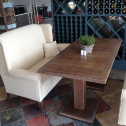 E3 Office Interiors - Nowoczesna sofa z wysokim oparciem w restauracji La Riva, obok drewniany stół z dekoracją roślinną i regał na wino w tle. Projekt Joanna Kukulska.