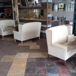E3 Office Interiors - Eleganckie, kremowe sofy z poduszkami i drewnianymi stolikami w restauracji z akwarium w tle. Nietypowa podłoga z płytek w różnych kolorach i wzorach.