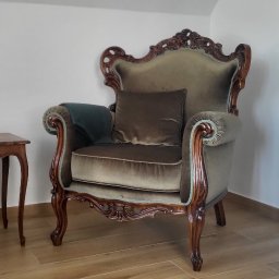 E3 Office Interiors - Elegancki fotel w stylu vintage, obity pluszowym welurem w odcieniach zieleni i brązu, z rzeźbionymi drewnianymi elementami, na tle jasnego wnętrza z drewnianą podłogą.