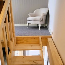 E3 Office Interiors - Kremowy fotel butikowy na tle szaro-białej ściany, widziany z perspektywy drewnianych schodów. Ujęcie z dołu, podkreślające unikalny kąt widzenia.