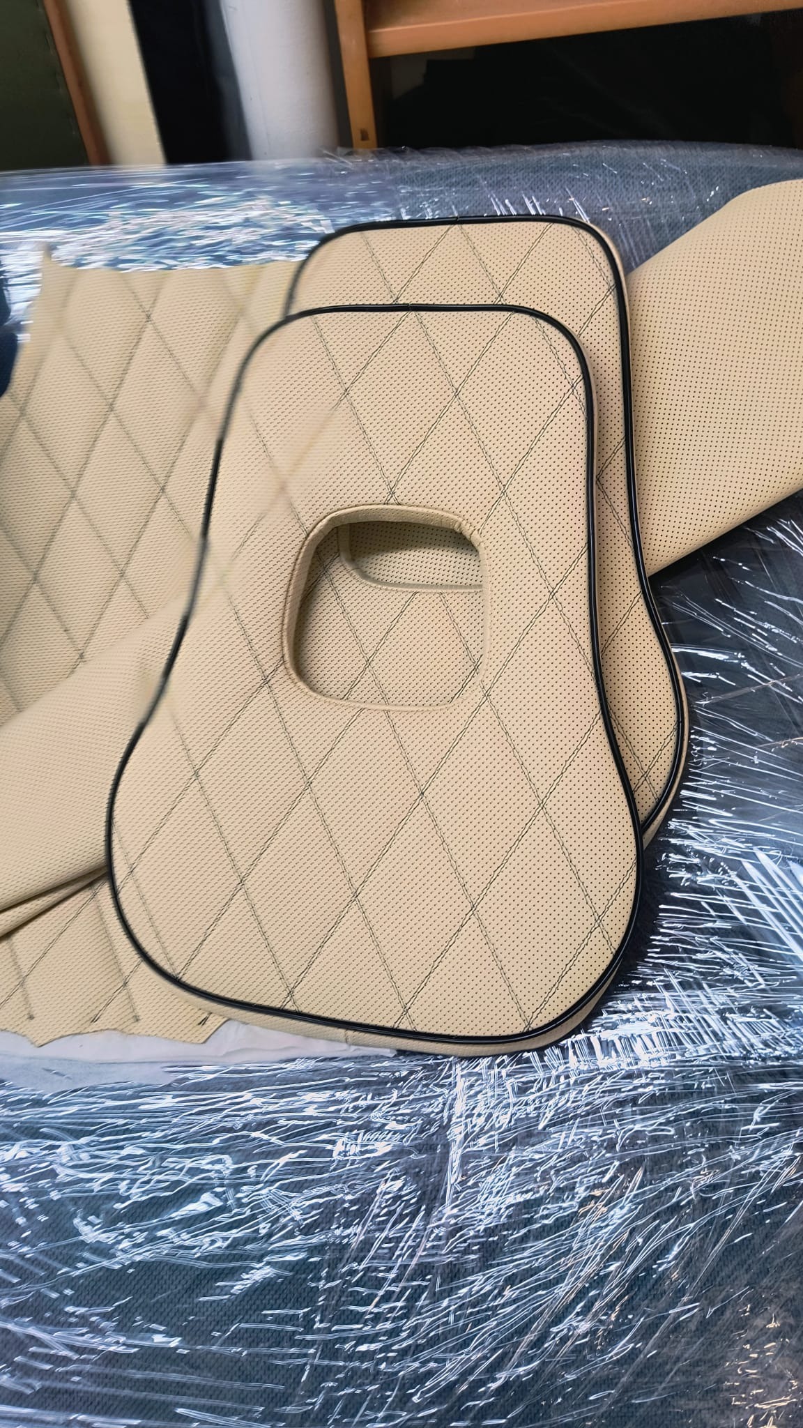 Beżowe, pikowane siedziska do Citroen AMI z czarną lamówką, leżące na folii. Widoczne otwory na zagłówki. Detal tapicerki samochodowej.