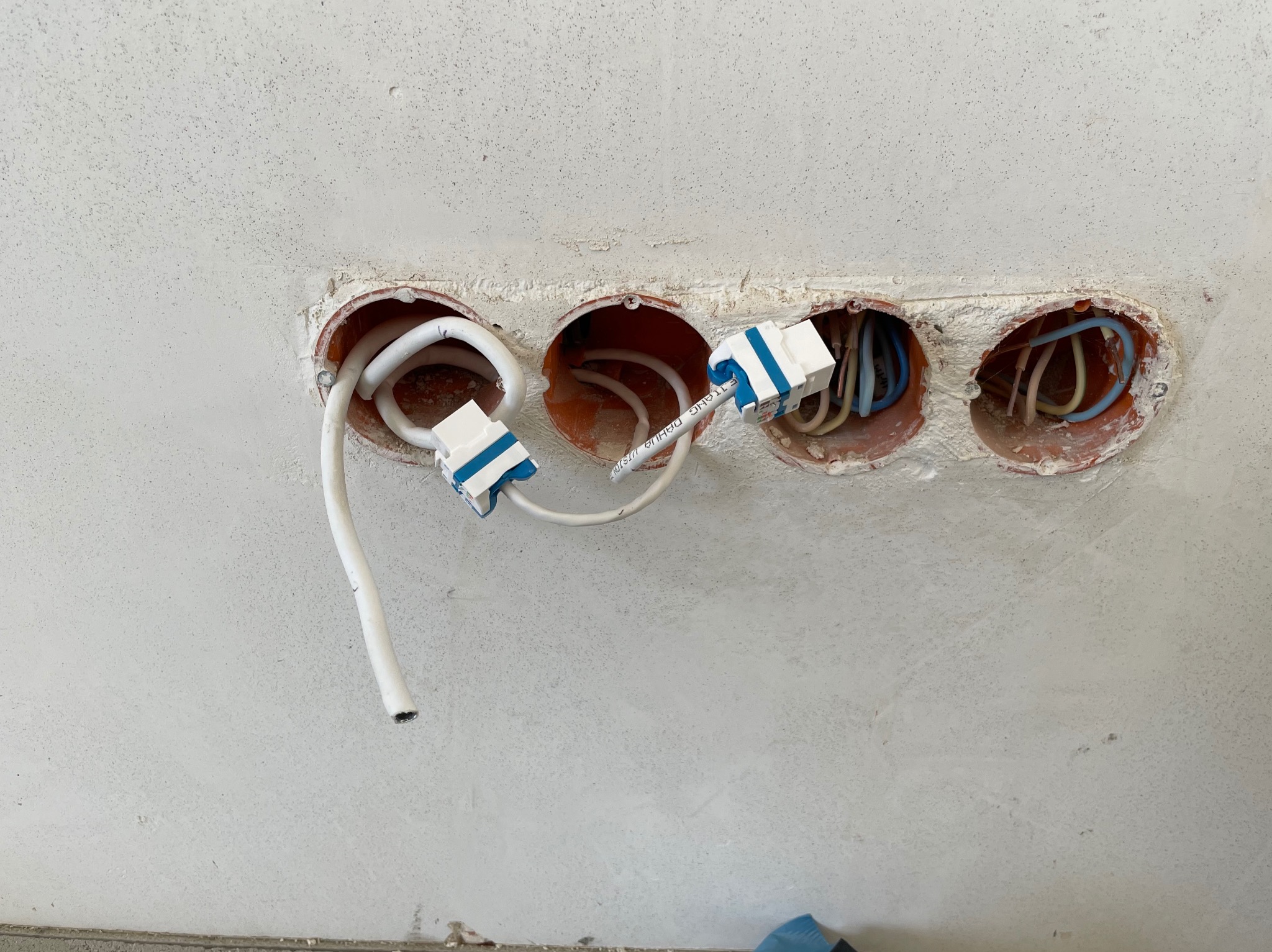 Cztery okrągłe puszki instalacyjne w surowej ścianie, z widocznymi przewodami i złączkami. Widok z bliska na instalację elektryczną w trakcie prac wykończeniowych.