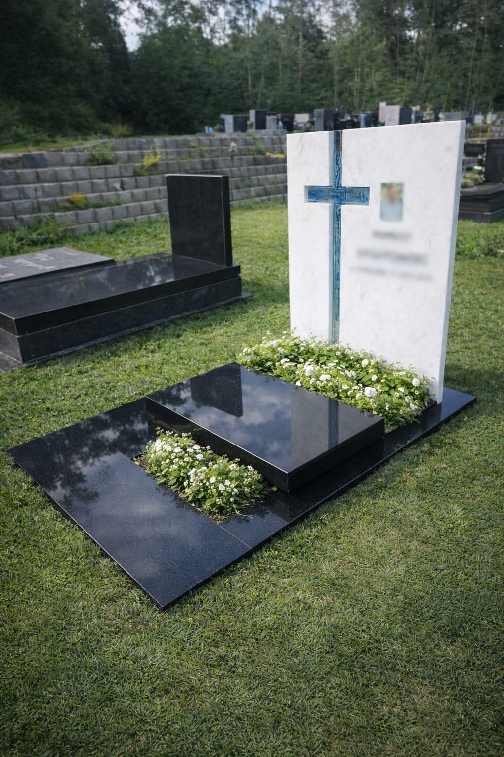 Czarny, polerowany nagrobek z białym krzyżem i kwiatami na trawie, na tle innych nagrobków i zieleni. Widok z bliska, spokojna atmosfera.