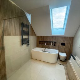 MIK-BUD Mikołaj Patrzała - Nowoczesna łazienka na poddaszu z drewnianą okładziną, białą wanną i oknem dachowym. Minimalistyczny design, jasne płytki podłogowe, grzejnik drabinkowy.