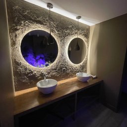 MIK-BUD Mikołaj Patrzała - Nowoczesna łazienka z dwoma okrągłymi lustrami z podświetleniem LED, umywalkami nablatowymi i blatem z drewna. Ściana z fakturą, wiszące lampy.