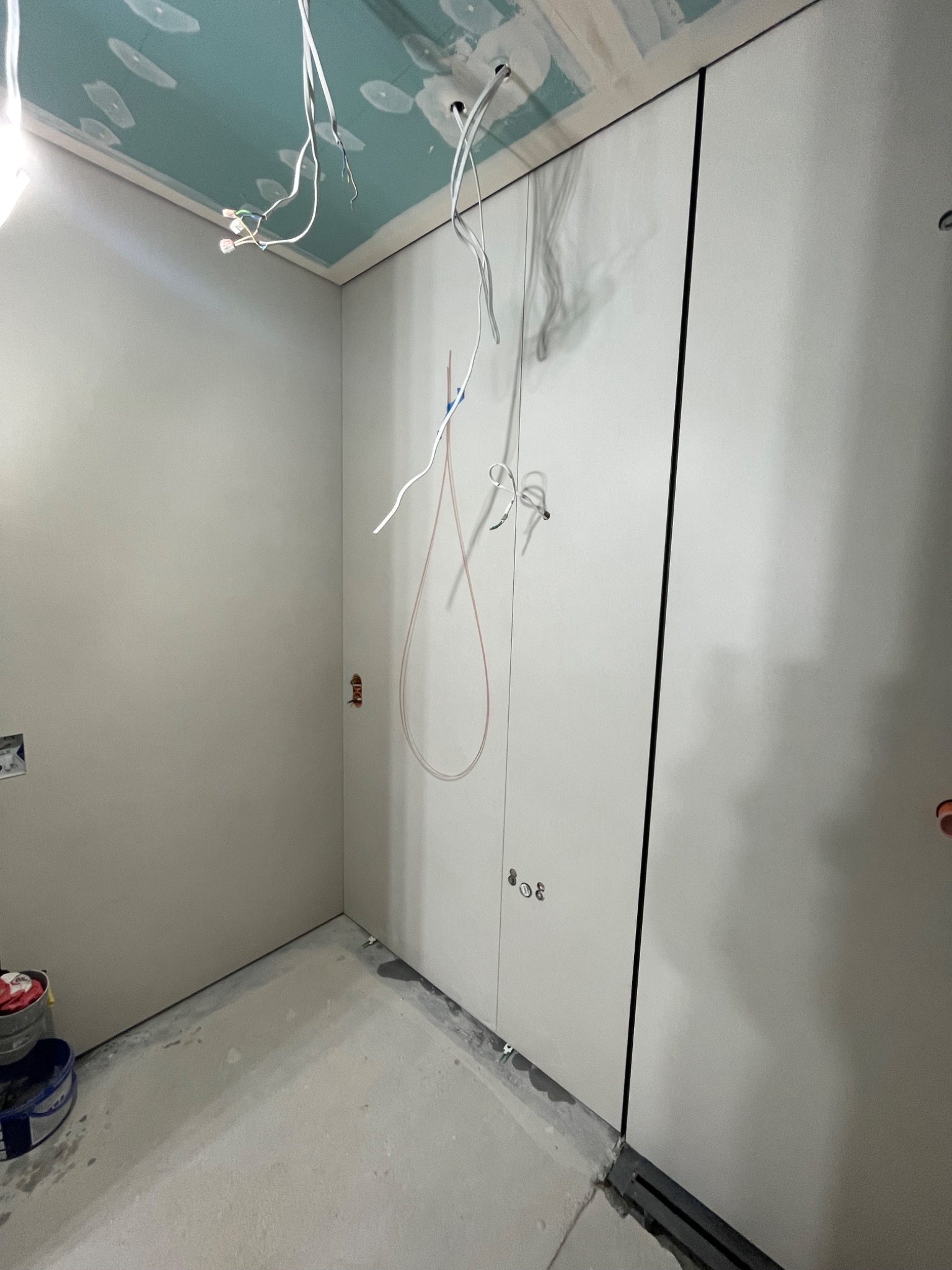 Surowa łazienka w trakcie wykończenia: płyty karton-gips na ścianach, widoczne kable elektryczne, sufit w kolorze turkusowym. Minimalistyczny odpływ liniowy w podłodze.
