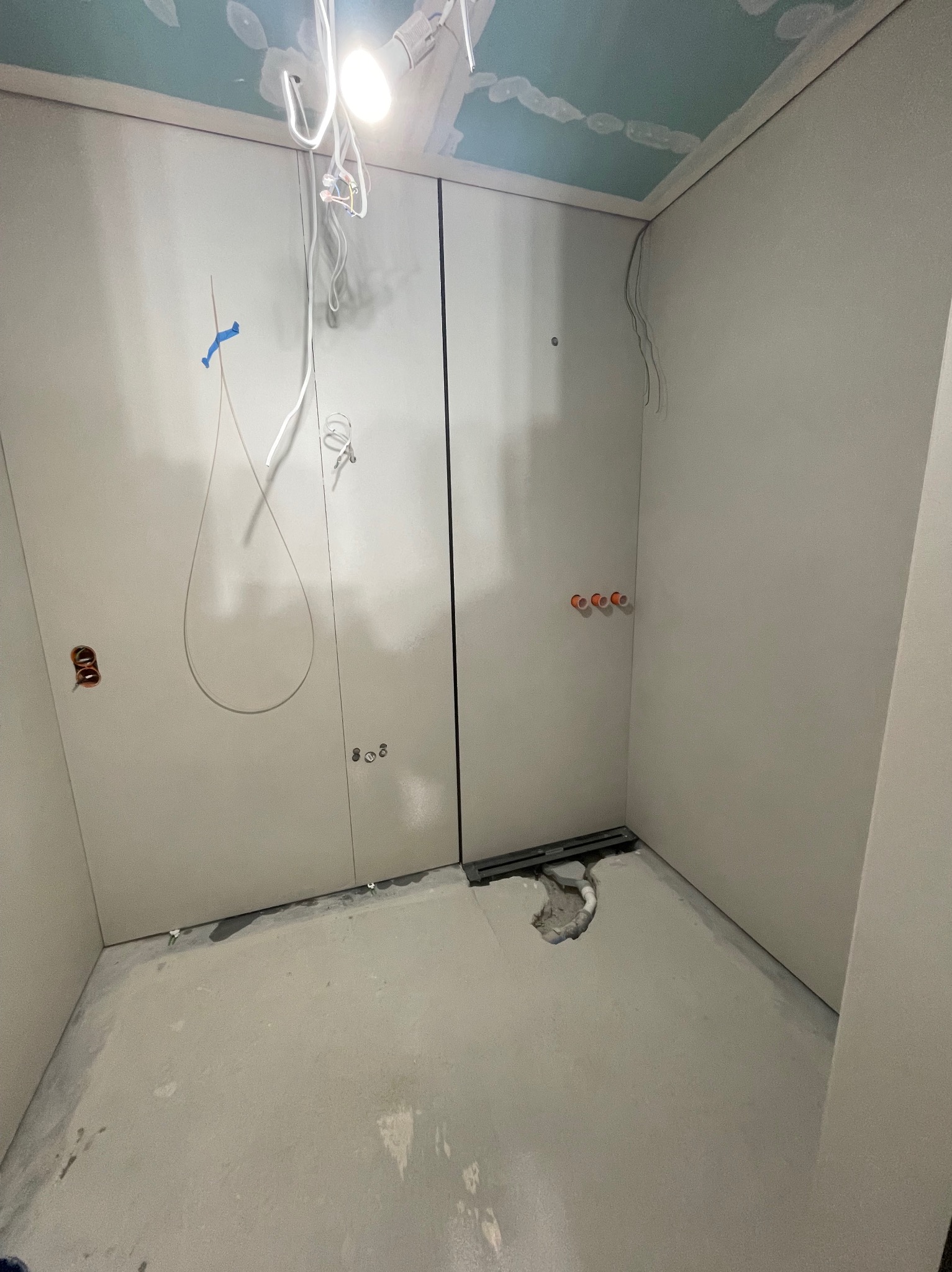 Łazienka w trakcie remontu: ściany wykończone płytami, widoczne instalacje elektryczne i hydrauliczne, odpływ liniowy. Sufit z dekoracyjnym malowaniem w odcieniach błękitu.