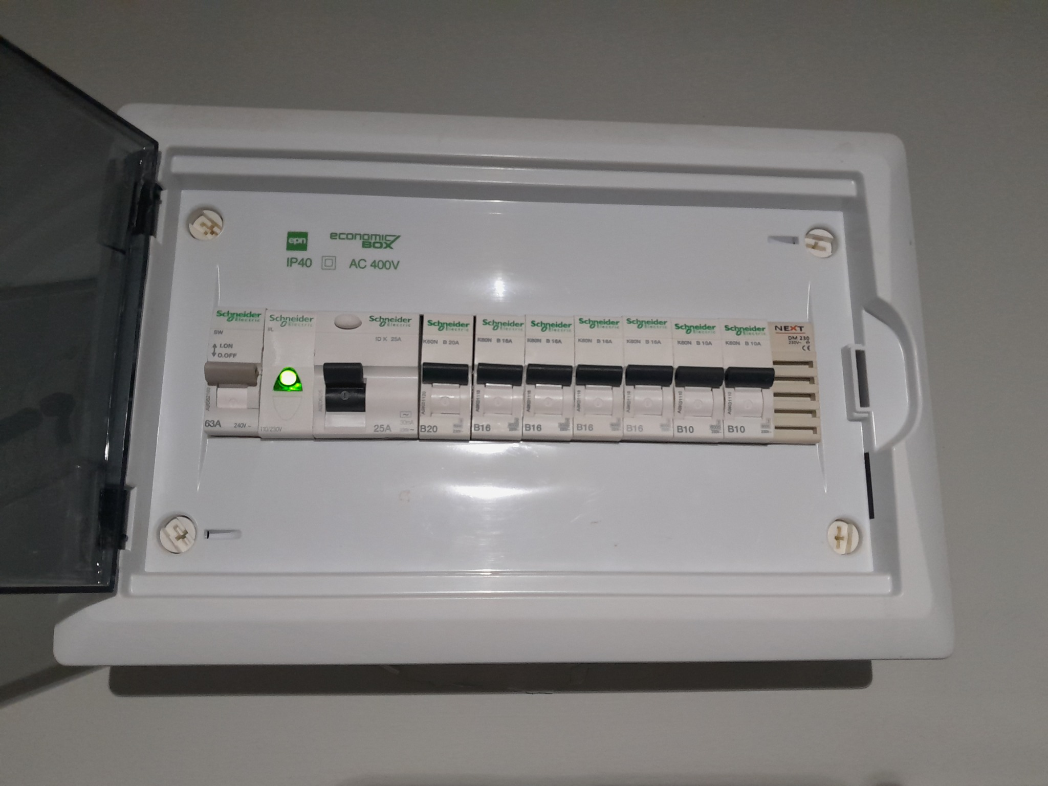 Otwarta skrzynka elektryczna Schneider z bezpiecznikami, widoczny włączony obwód. Instalacja wewnątrz pomieszczenia, z bliska.