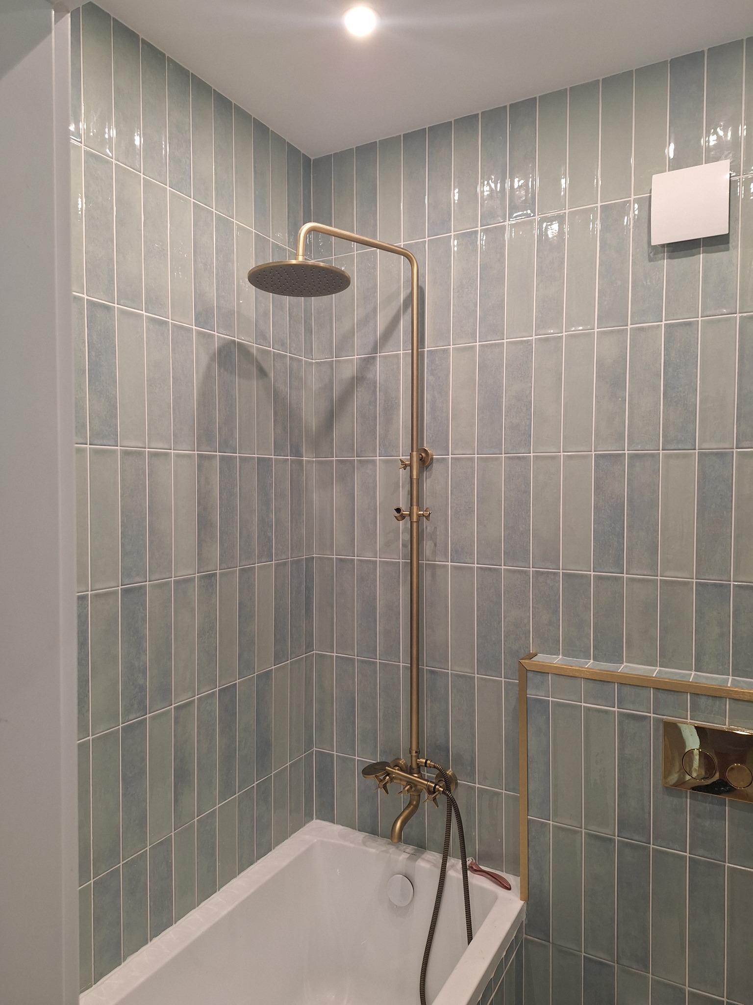 Wykończona łazienka z wanną, baterią w stylu retro i pionowymi, błękitnymi płytkami. Widoczny fragment wentylacji i detale w kolorze złotym.