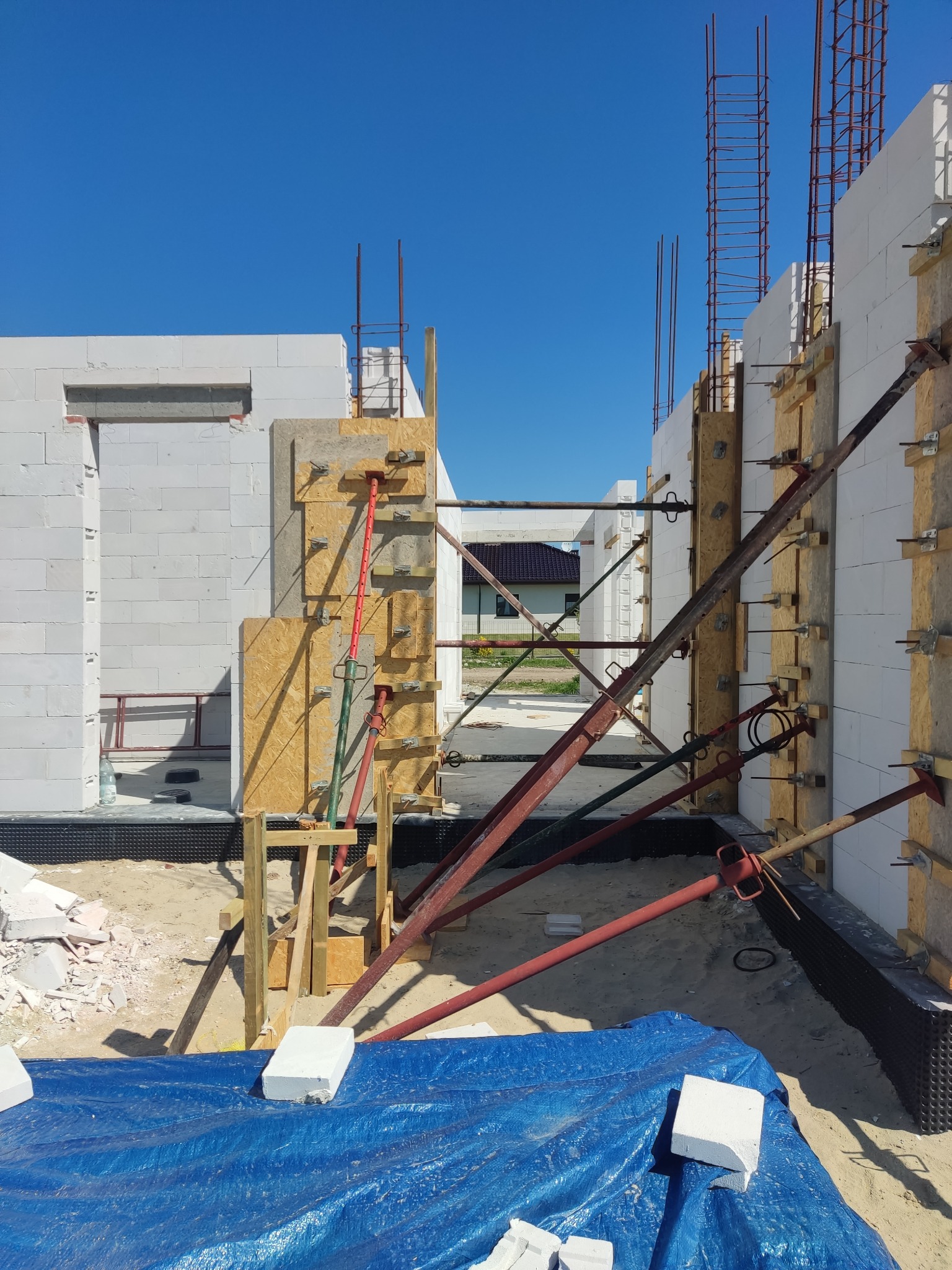 Wznoszenie ścian z betonu komórkowego Ytong, zbrojenie pionowe, szalunki drewniane, podpory stalowe. Budowa domu w trakcie realizacji, błękitne niebo.