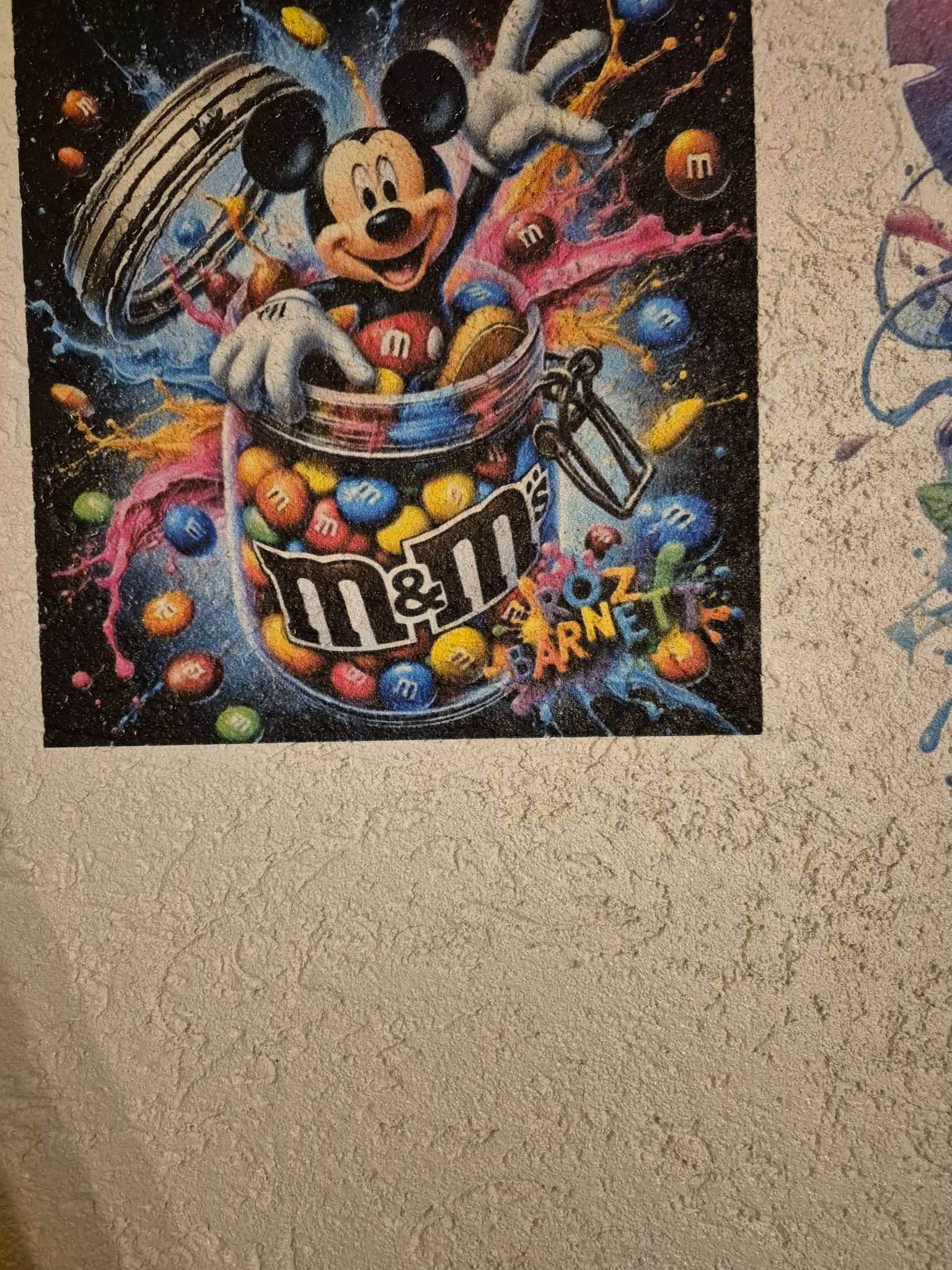 Kolorowa grafika na ścianie z fakturą, przedstawiająca postać z kreskówki w słoiku z cukierkami, w stylu graffiti. Widoczne detale i żywe barwy.