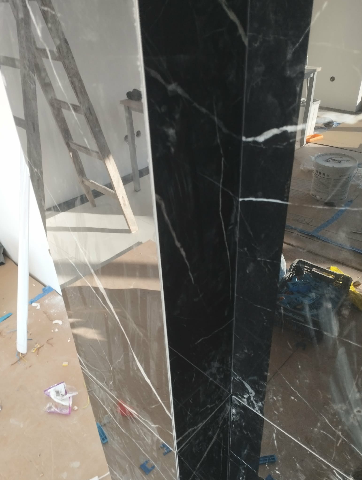 Ukończona kolumna z czarno-białych płytek imitujących marmur, widoczna drabina i akcesoria glazurnicze w tle, co sugeruje świeżo zakończone prace wykończeniowe.