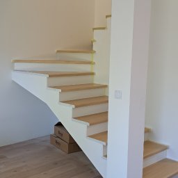 WOODEN ART SPÓŁKA Z OGRANICZONĄ ODPOWIEDZIALNOŚCIĄ - Nowoczesne schody drewniane z białymi podstopnicami i drewnianymi stopniami, zabezpieczone taśmą malarską, w jasnym wnętrzu. Widoczne kartony i podłoga z paneli.