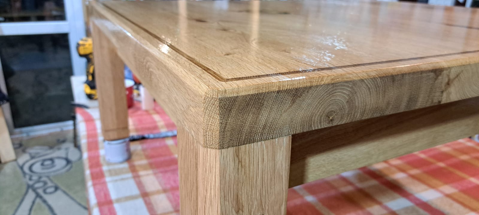 Lakierowany stolik kawowy z litego dębu, widoczne detale połączeń i usłojenie drewna. W tle narzędzia i akcesoria stolarskie.