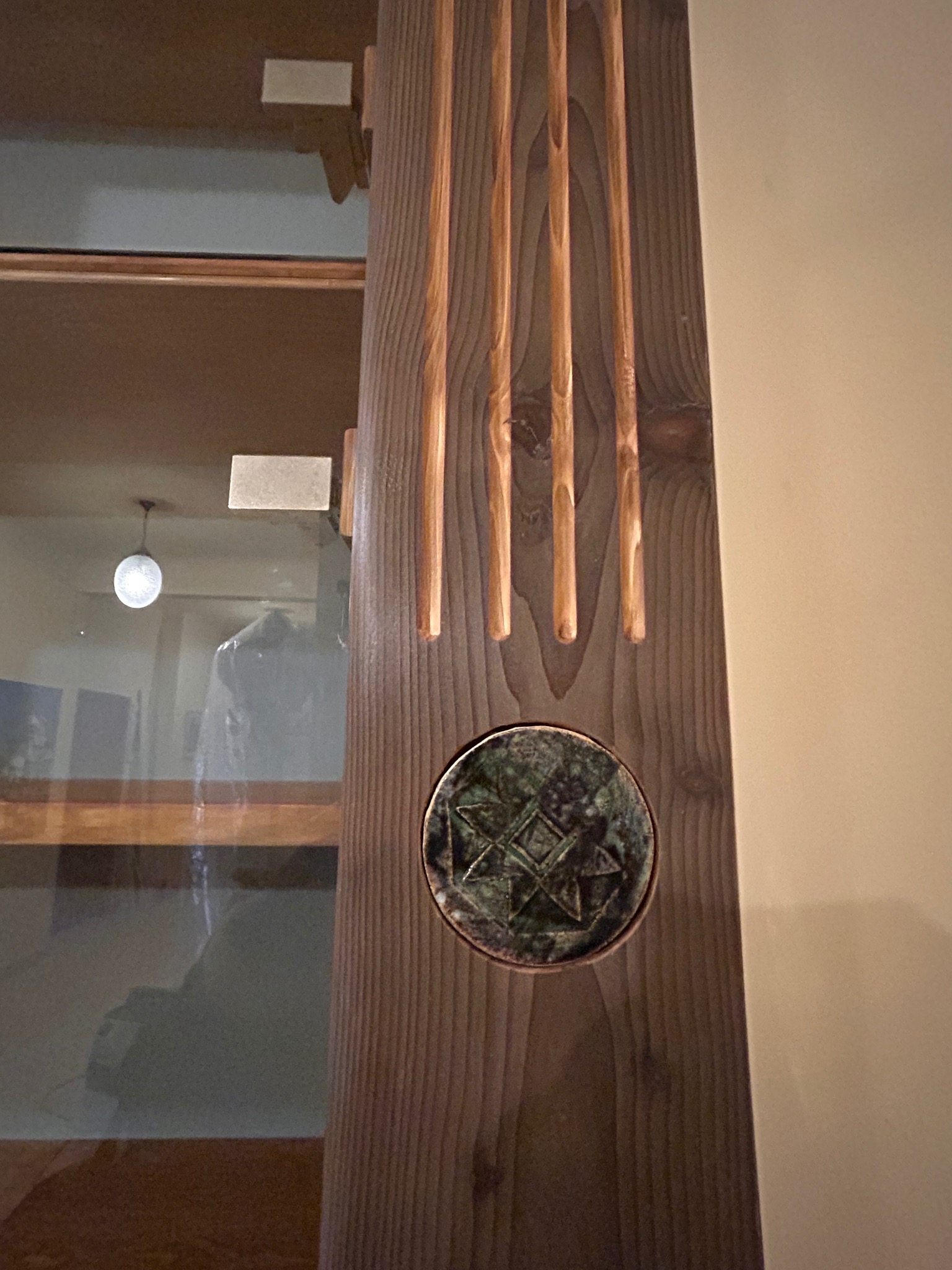 Detal drewnianej konstrukcji z dekoracyjnymi frezami i okrągłym, zdobionym elementem. Widoczne usłojenie drewna i odbicie wnętrza w szklanej powierzchni.