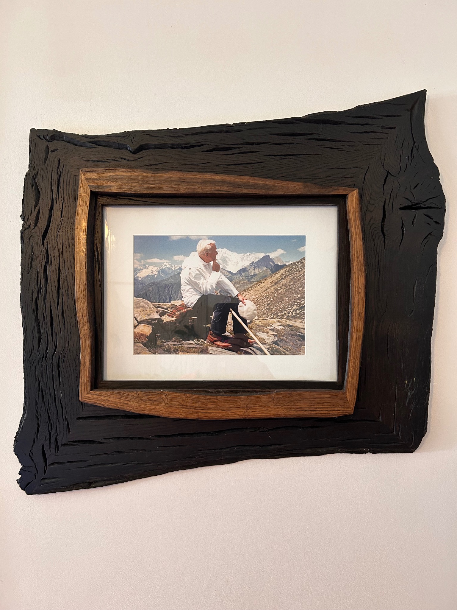 Ręcznie wykonana rama z ciemnego drewna otaczająca zdjęcie górskiego krajobrazu z siedzącą osobą, unikalna faktura drewna, naturalny wygląd.
