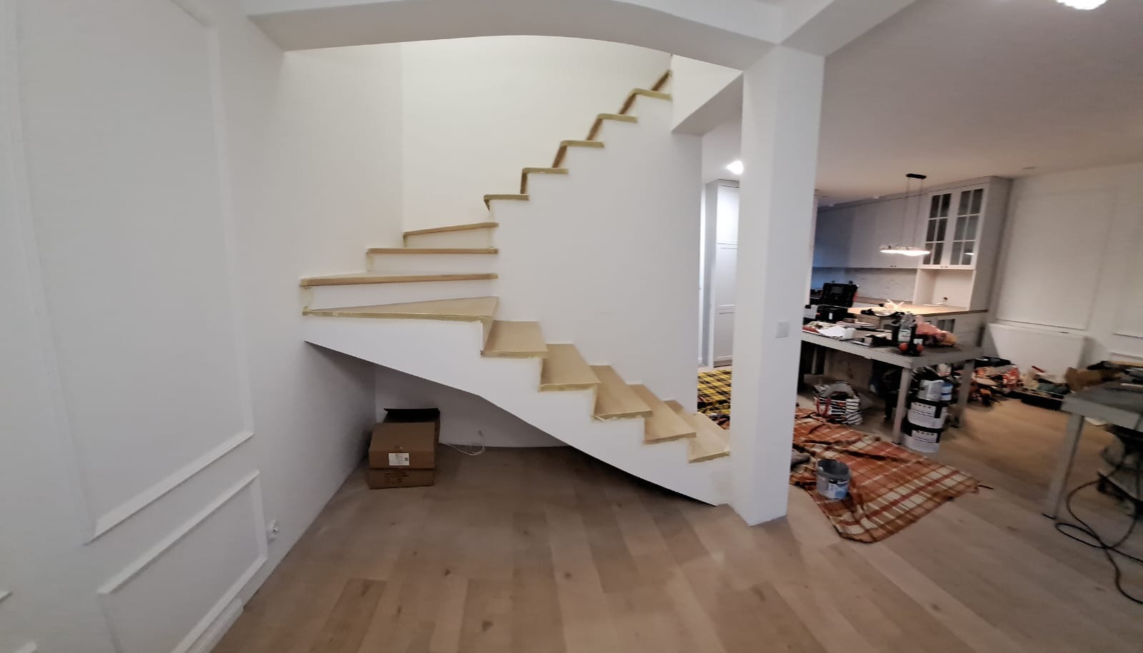 Spiralne schody z jasnego drewna w trakcie montażu, widoczne zabezpieczenia na stopniach. W tle pomieszczenie z narzędziami i elementami wykończenia wnętrz.