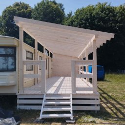 Monstar - Drewniana dobudówka z zadaszeniem przyczepy kempingowej, jasne drewno, schody wejściowe, widok z zewnątrz w słoneczny dzień, drzewa w tle.