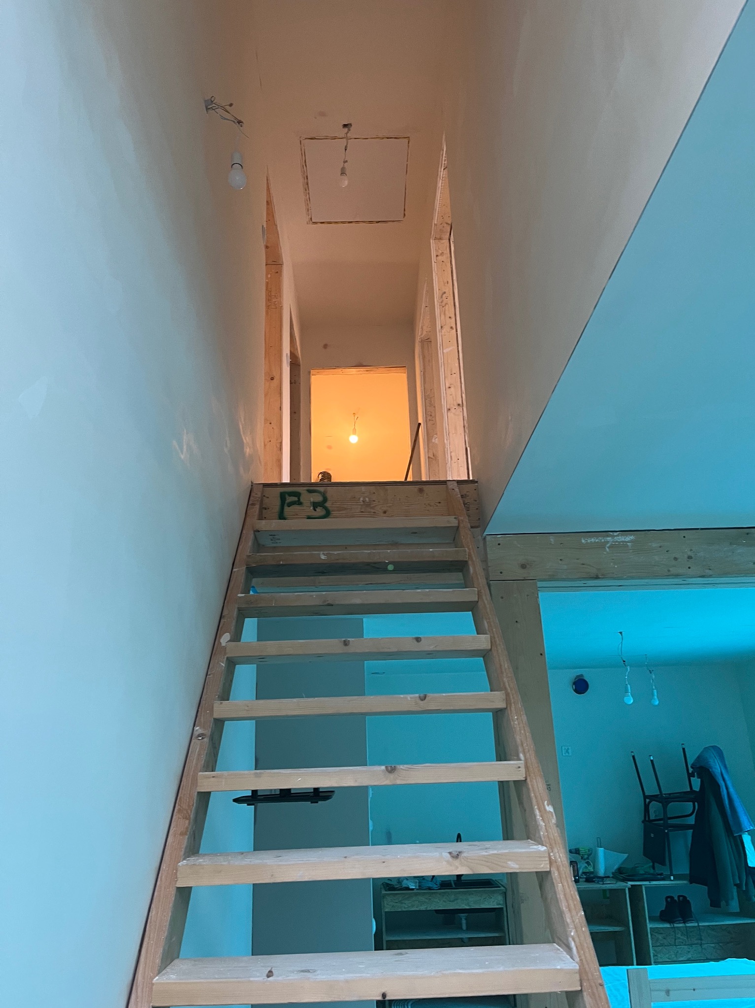 Wnętrze w trakcie prac wykończeniowych: drewniane schody prowadzą na antresolę, ściany przygotowane pod malowanie, widoczne elementy konstrukcyjne.