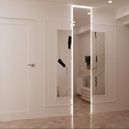 SanSi Design - Korytarz w neutralnych barwach z lustrem z podświetleniem LED, dekoracyjnymi obrazami w ramkach i drewnianymi drzwiami. Parkiet na podłodze.