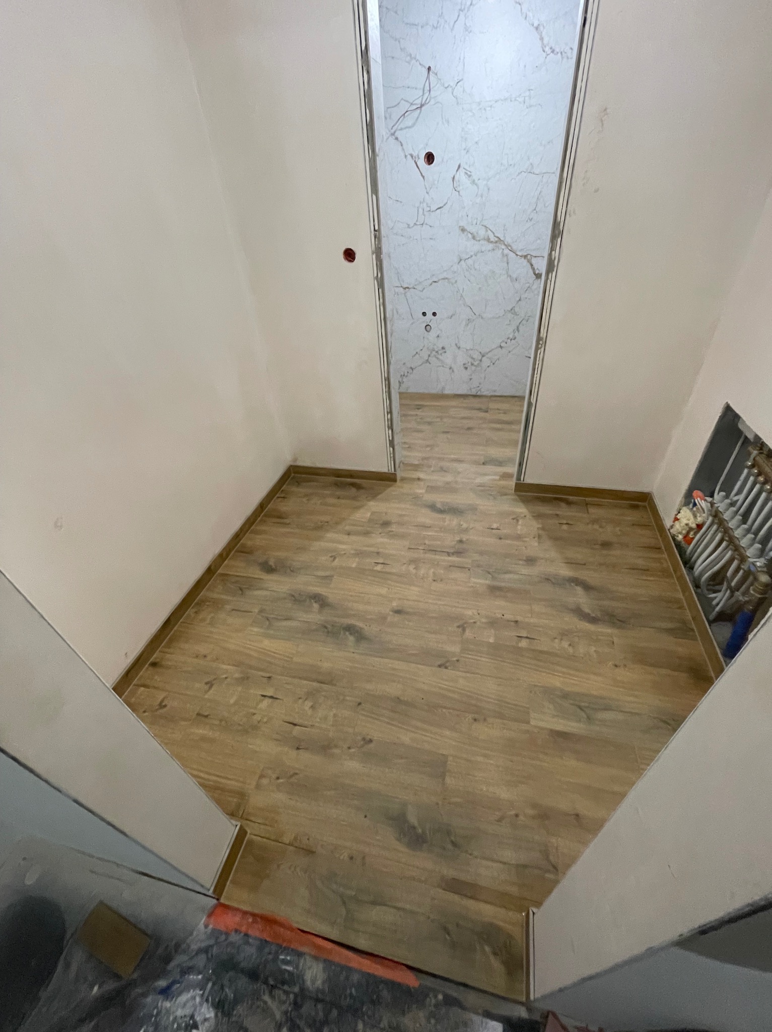 Ukończona podłoga z paneli drewnopodobnych w korytarzu, widok na wykończoną łazienkę z marmurowymi płytkami w Frydmanie. Widoczna instalacja ogrzewania podłogowego.