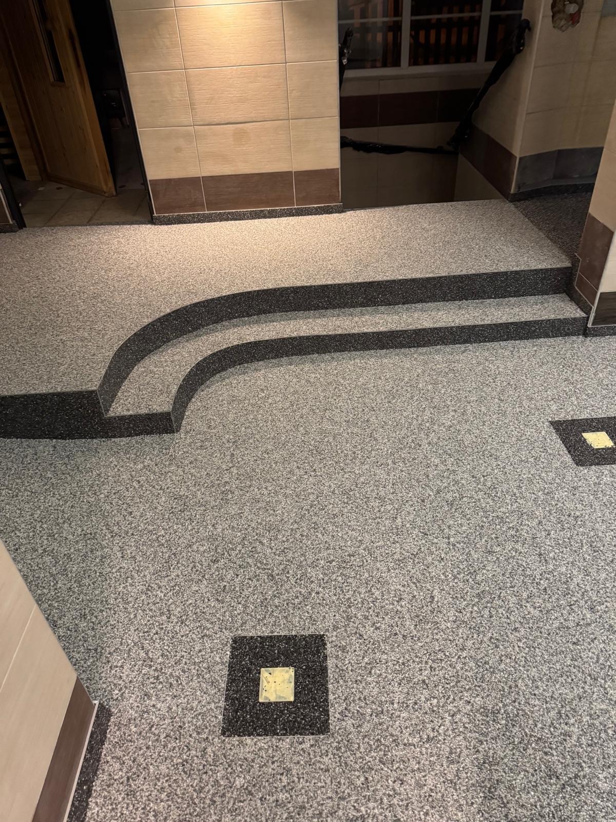 Szara posadzka żywiczna z czarnymi schodami i kwadratowymi elementami dekoracyjnymi wewnątrz budynku. Widok z góry na wykończone wnętrze.