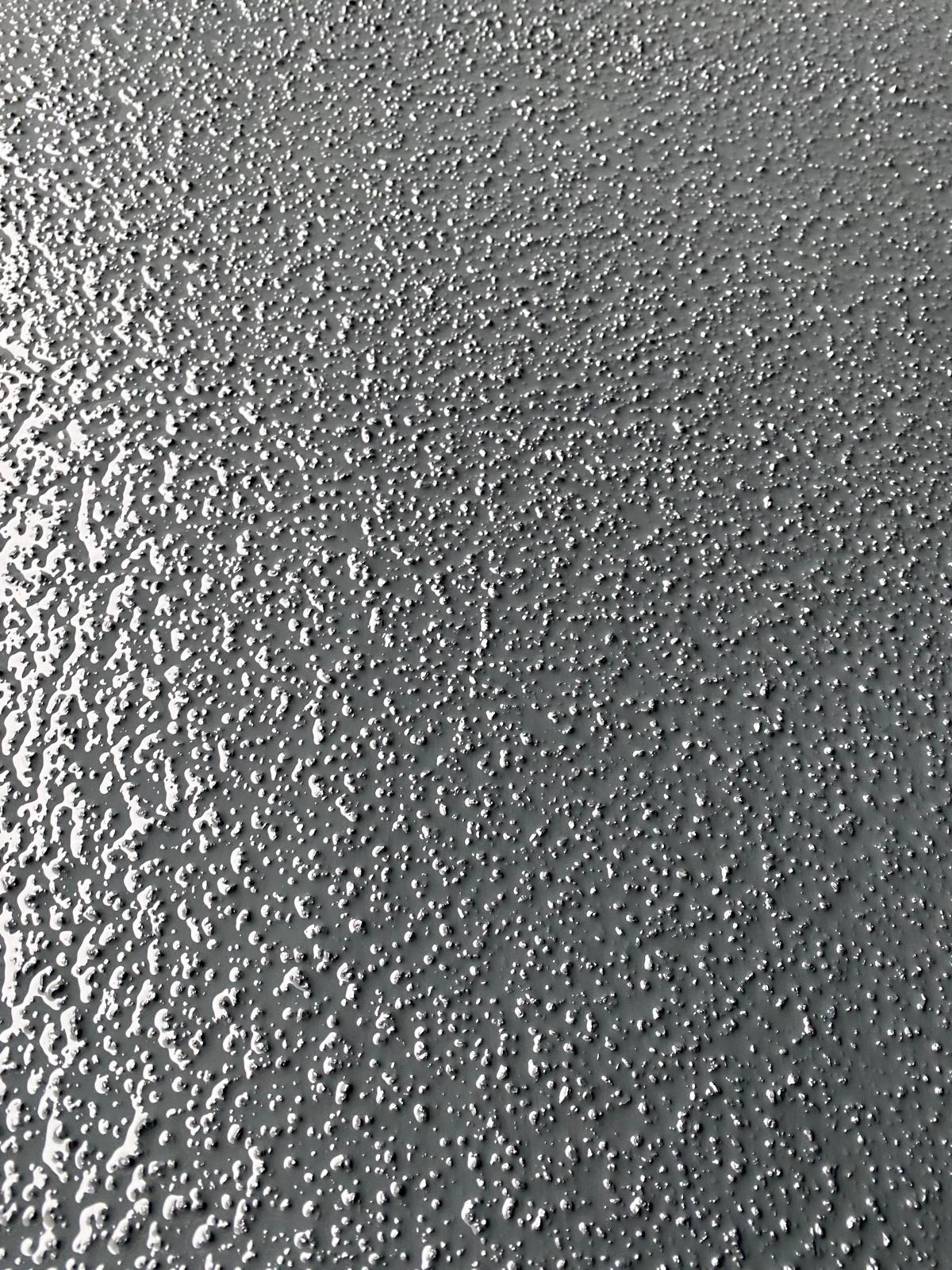 Szara, błyszcząca posadzka żywiczna z wyraźną, nieregularną fakturą. Widoczne drobne nierówności i refleksy światła podkreślające strukturę powierzchni.