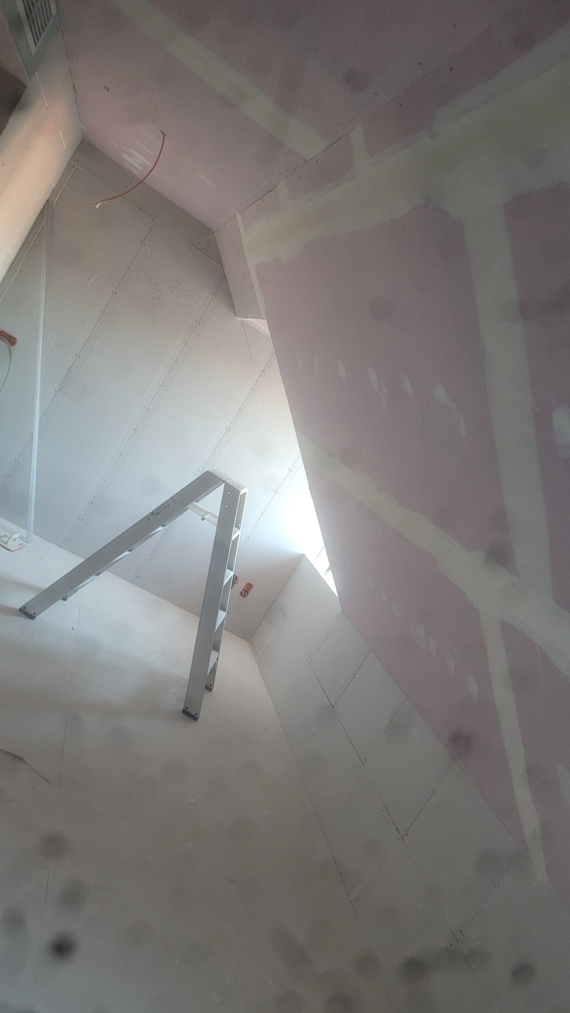 Skośne poddasze z płytami, częściowo wyszpachlowane, z widoczną drabiną. Praca w toku, surowe wykończenie, widoczne łączenia płyt. Ujęcie z dołu, oświetlenie naturalne.