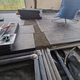 Zeta Profesjonalne Posadzki - Montaż ogrzewania podłogowego: rury grzewcze, izolacja termiczna i podsypka wyrównująca przed wylaniem posadzki. Widoczne narzędzia i materiały budowlane.