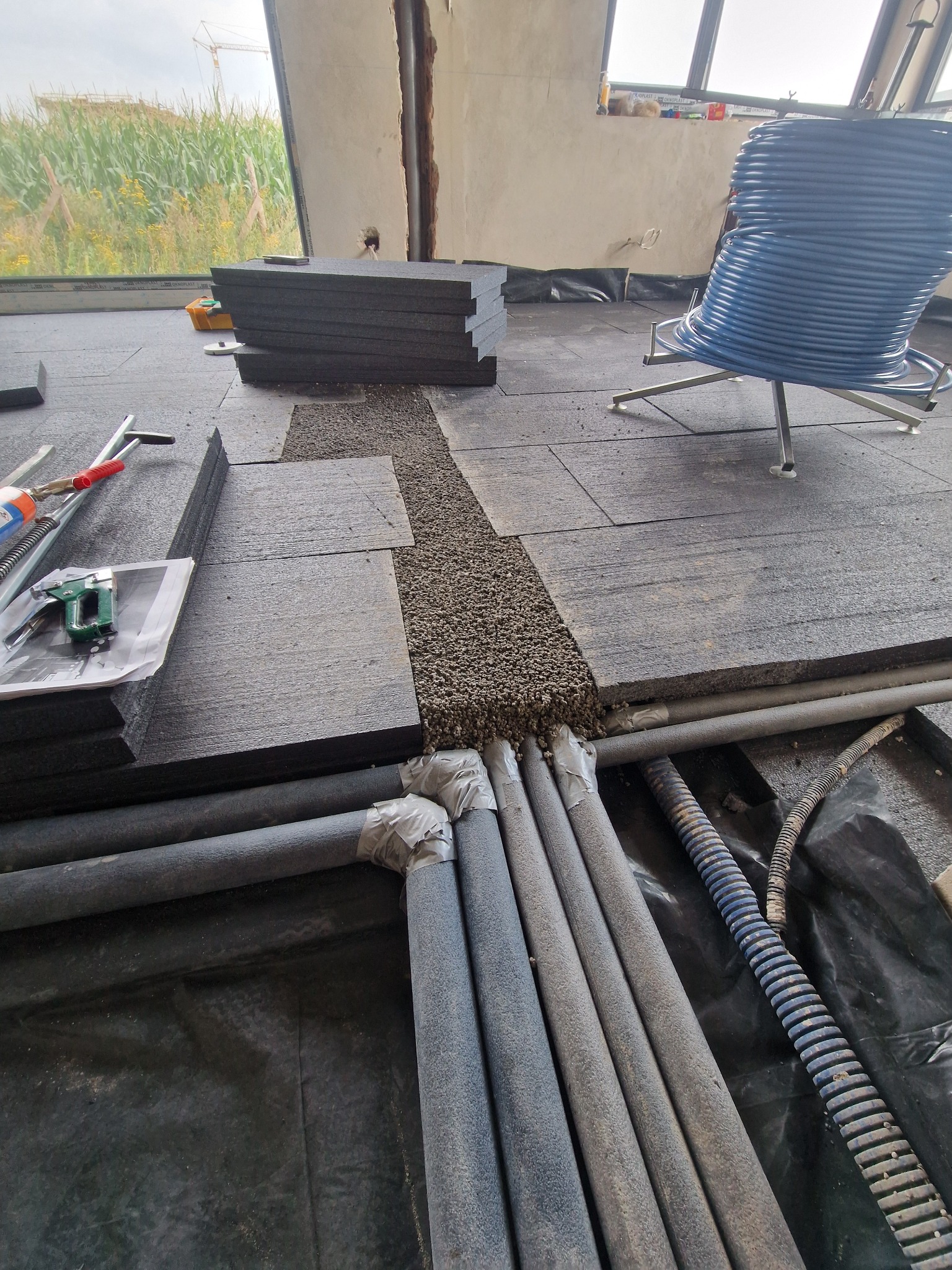 Montaż ogrzewania podłogowego: rury grzewcze, izolacja termiczna i podsypka wyrównująca przed wylaniem posadzki. Widoczne narzędzia i materiały budowlane.