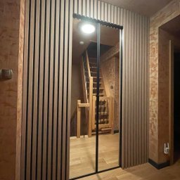 TPMU Agnieszka Rogala - Nowoczesna szafa wnękowa z lustrzanymi drzwiami przesuwnymi i drewnianymi lamelami, wkomponowana w korytarz z drewnianymi schodami i podłogą.