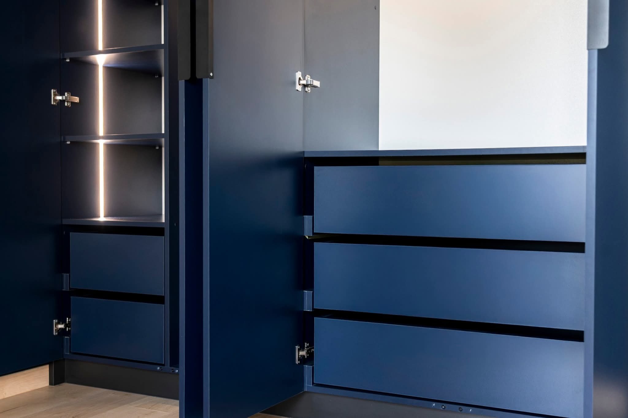 Niebieska szafa wnękowa z oświetleniem LED, widoczne półki i szuflady, otwarte drzwi ukazują wnętrze, minimalistyczny design.