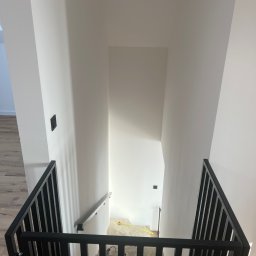 PHU Tomasz Dominikowski - Nowoczesna, czarna balustrada schodowa z pionowymi szczeblami, zamontowana w jasnym wnętrzu. Widok z góry na schody z drewnianymi stopniami i białe ściany.