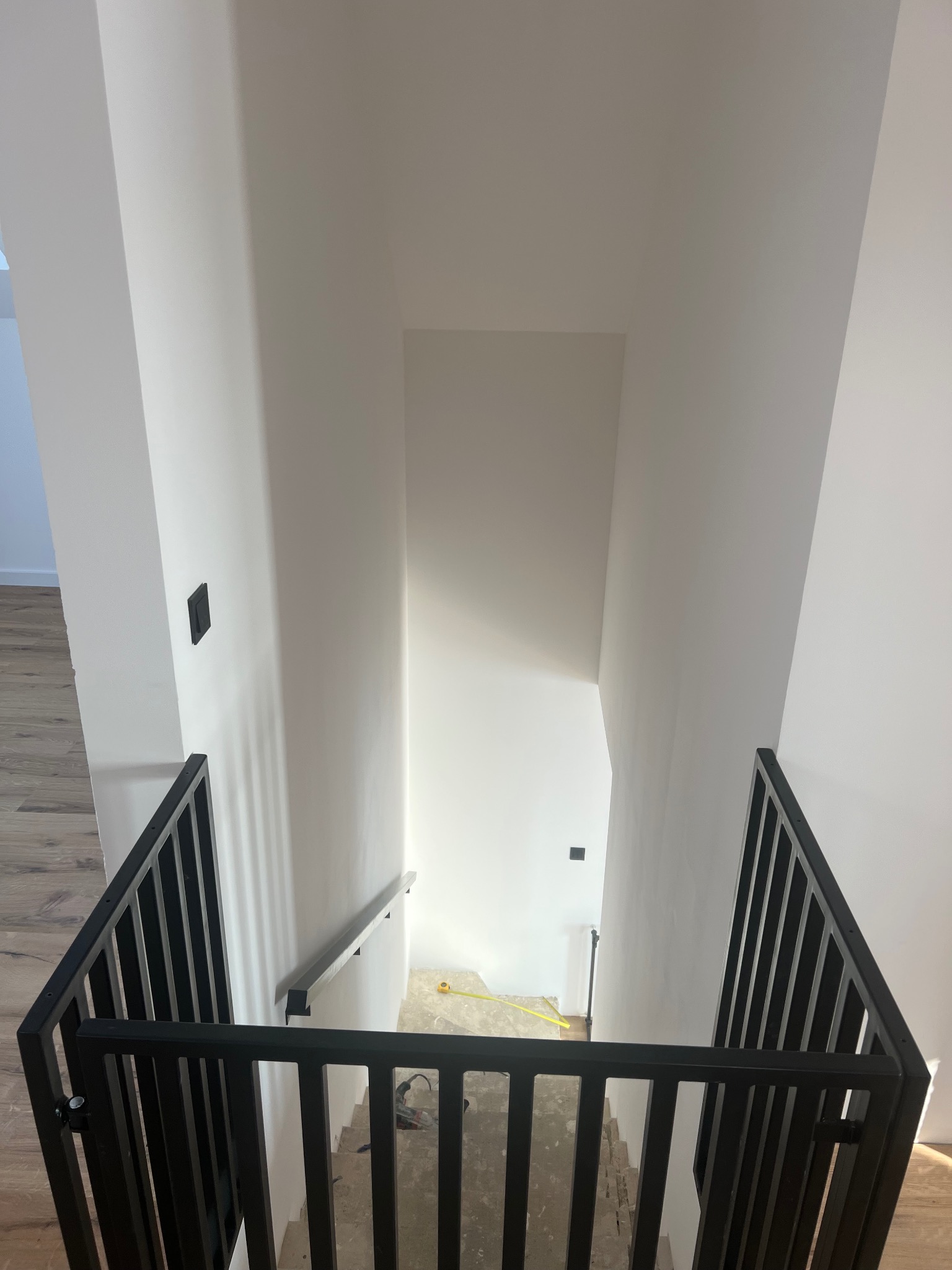 Nowoczesna, czarna balustrada schodowa z pionowymi szczeblami, zamontowana w jasnym wnętrzu. Widok z góry na schody z drewnianymi stopniami i białe ściany.