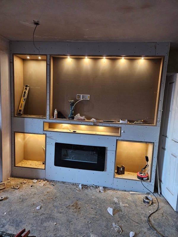 Wnęka z płyt kartonowo-gipsowych z wbudowanym kominkiem elektrycznym i oświetleniem LED, w trakcie montażu. Widoczne narzędzia i poziomica.